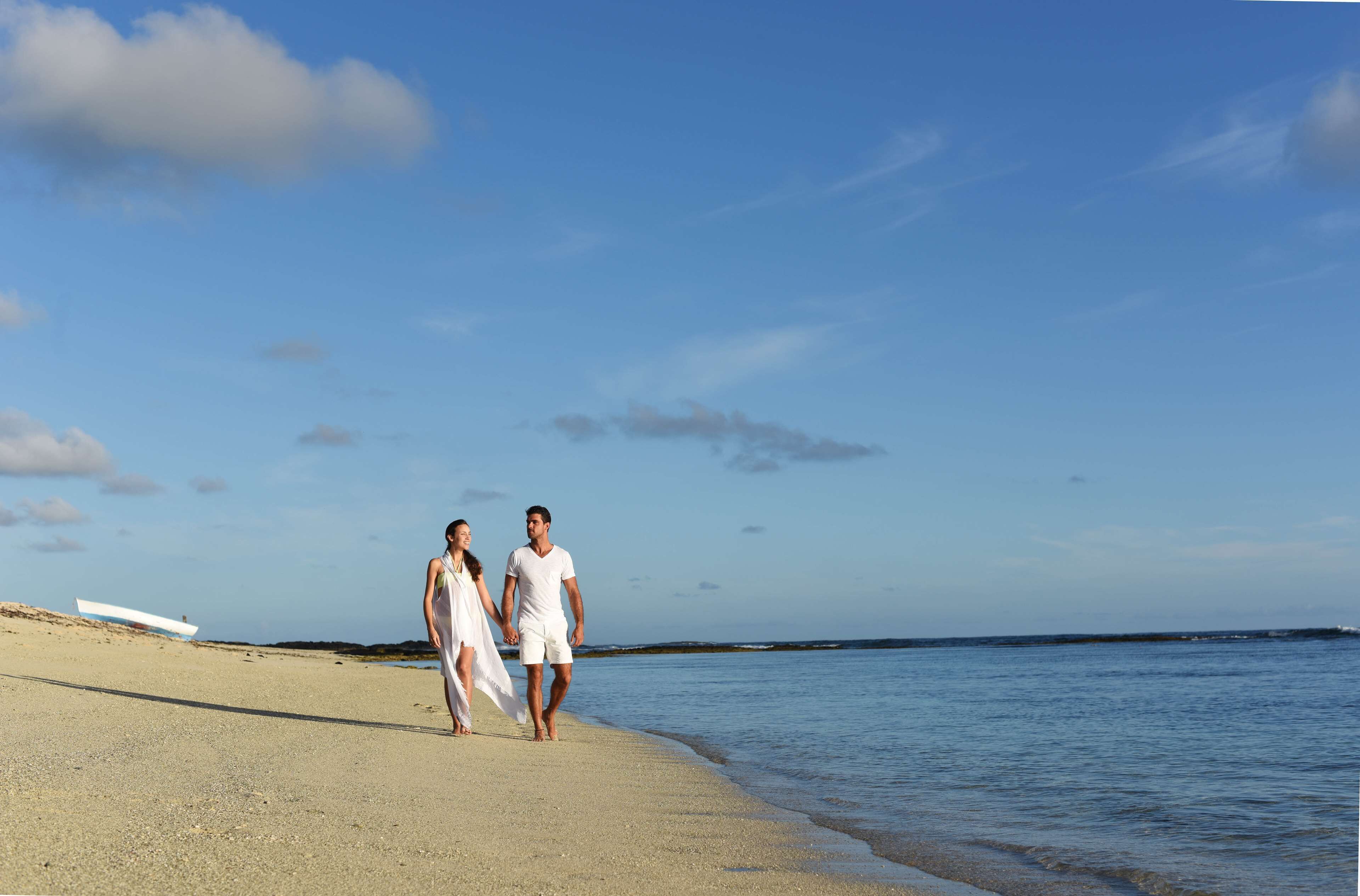 A couple walking on a beach with a boat in the background.