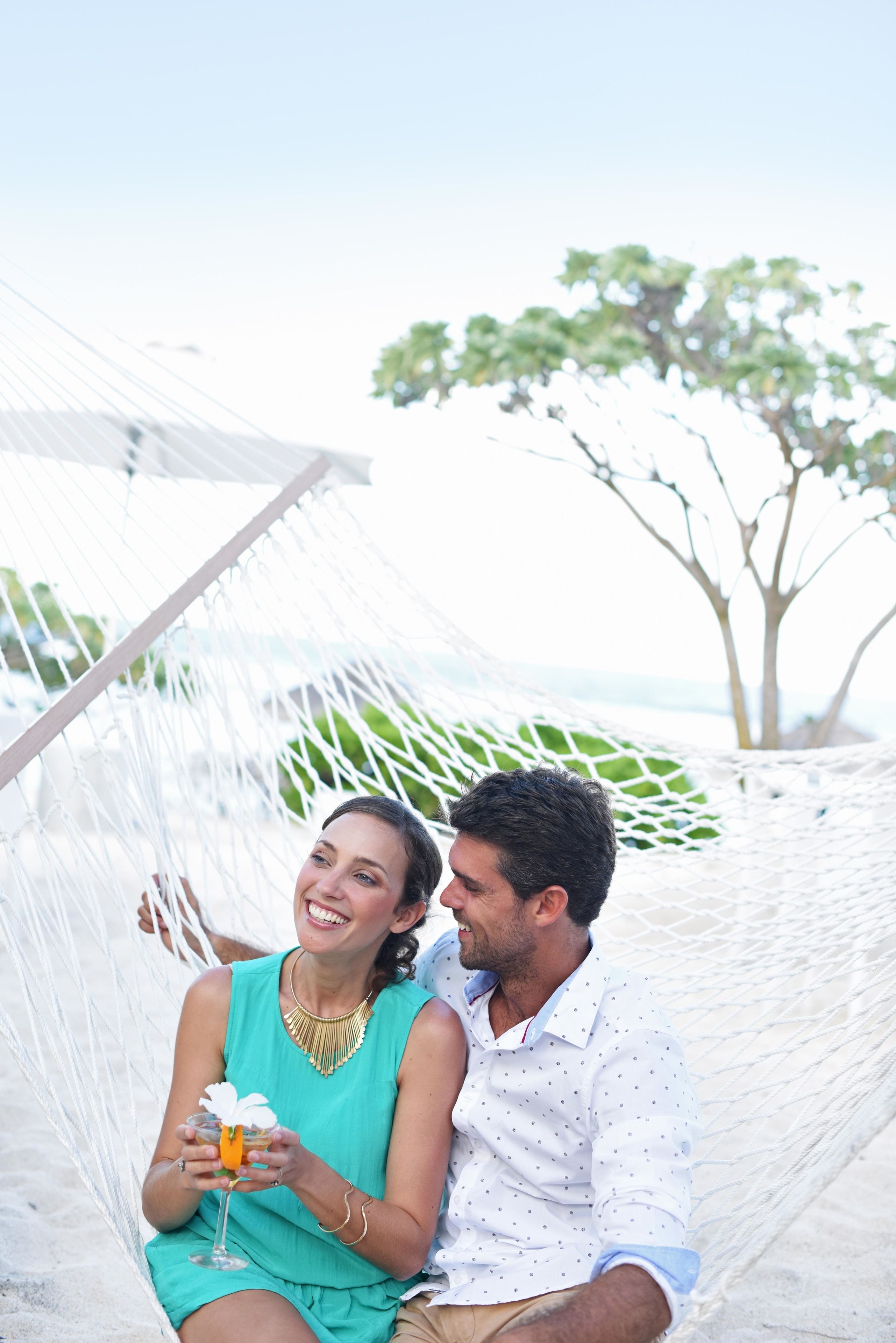 A hammock with two people sitting in it, a tree in the background, and a clear sky.