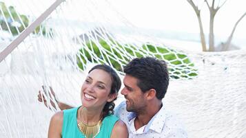 A hammock with two people sitting in it, a tree in the background, and a clear sky.