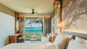 Habitación de hotel con cama, escritorio, silla y un amplio ventanal con vistas al océano.