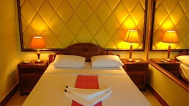 A hotel room with a large bed, two bedside lamps, a headboard with a diamond pattern, and a mirror on the wall. - Sky Park Guesthouse (Phnom Penh)