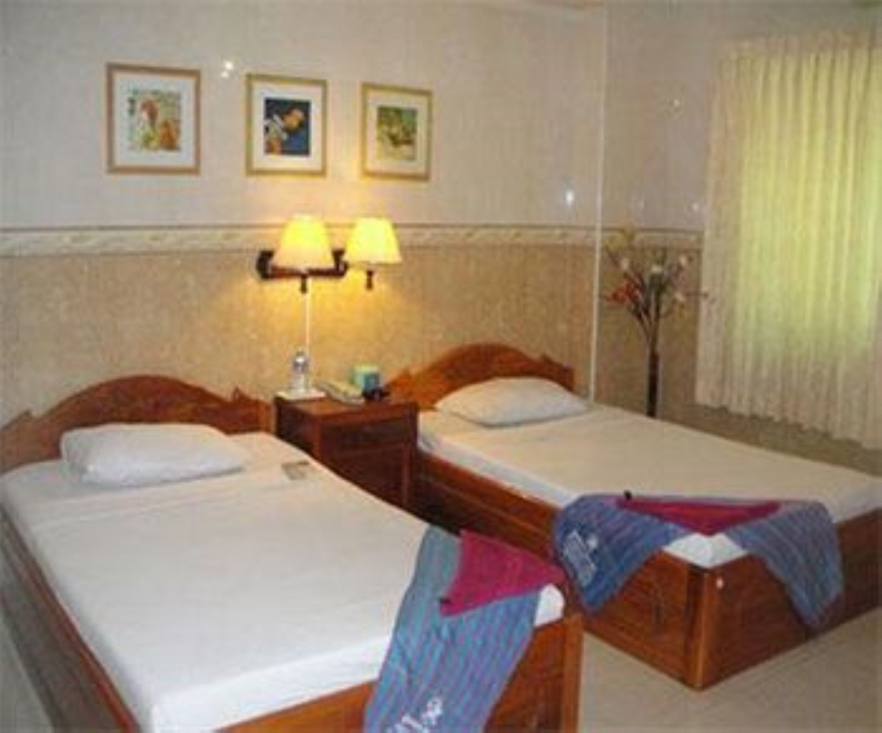 A hotel room with two single beds, a nightstand with a lamp, and a wall-mounted picture frame.
