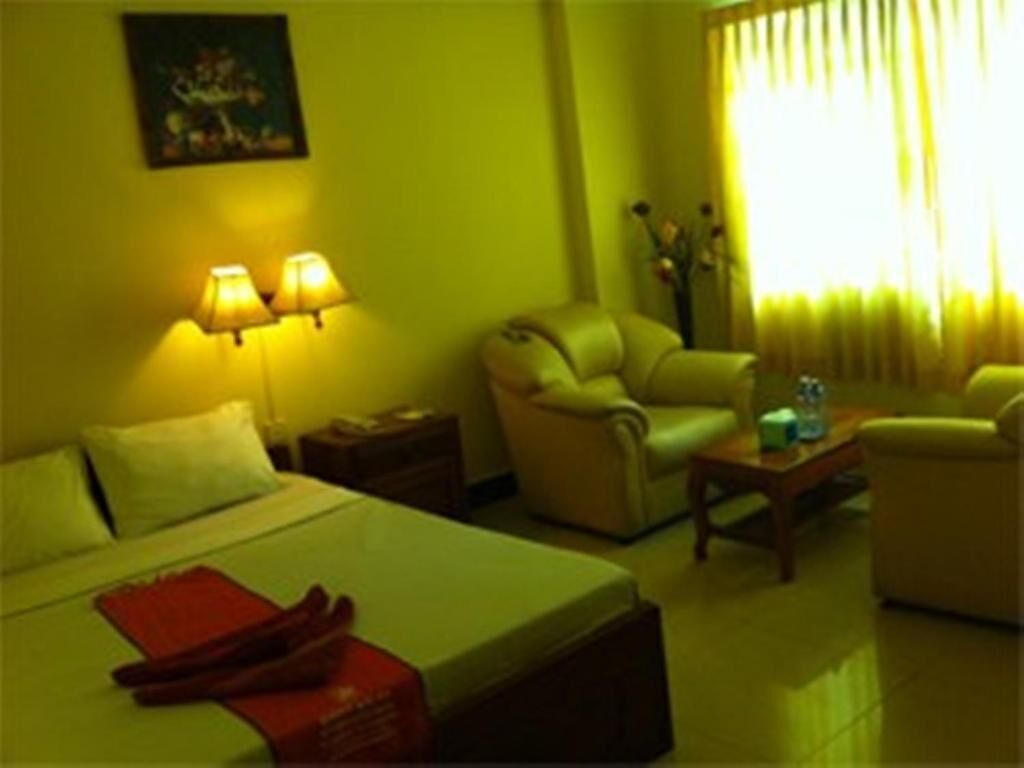 A hotel room with a bed, two bedside lamps, a sofa, a coffee table, and a window with curtains.