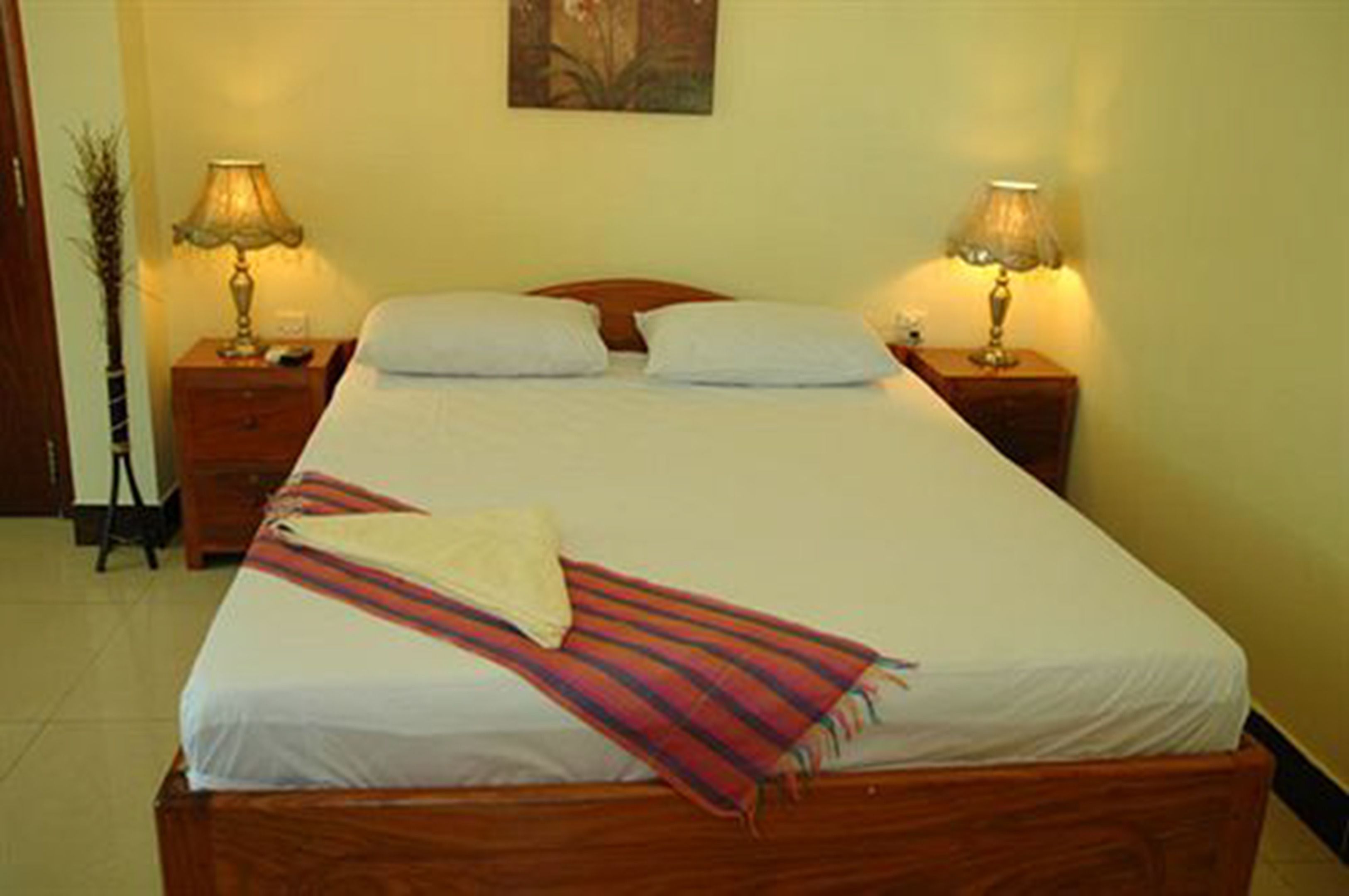 A neatly made bed with a striped blanket, two bedside lamps, and a painting on the wall.
