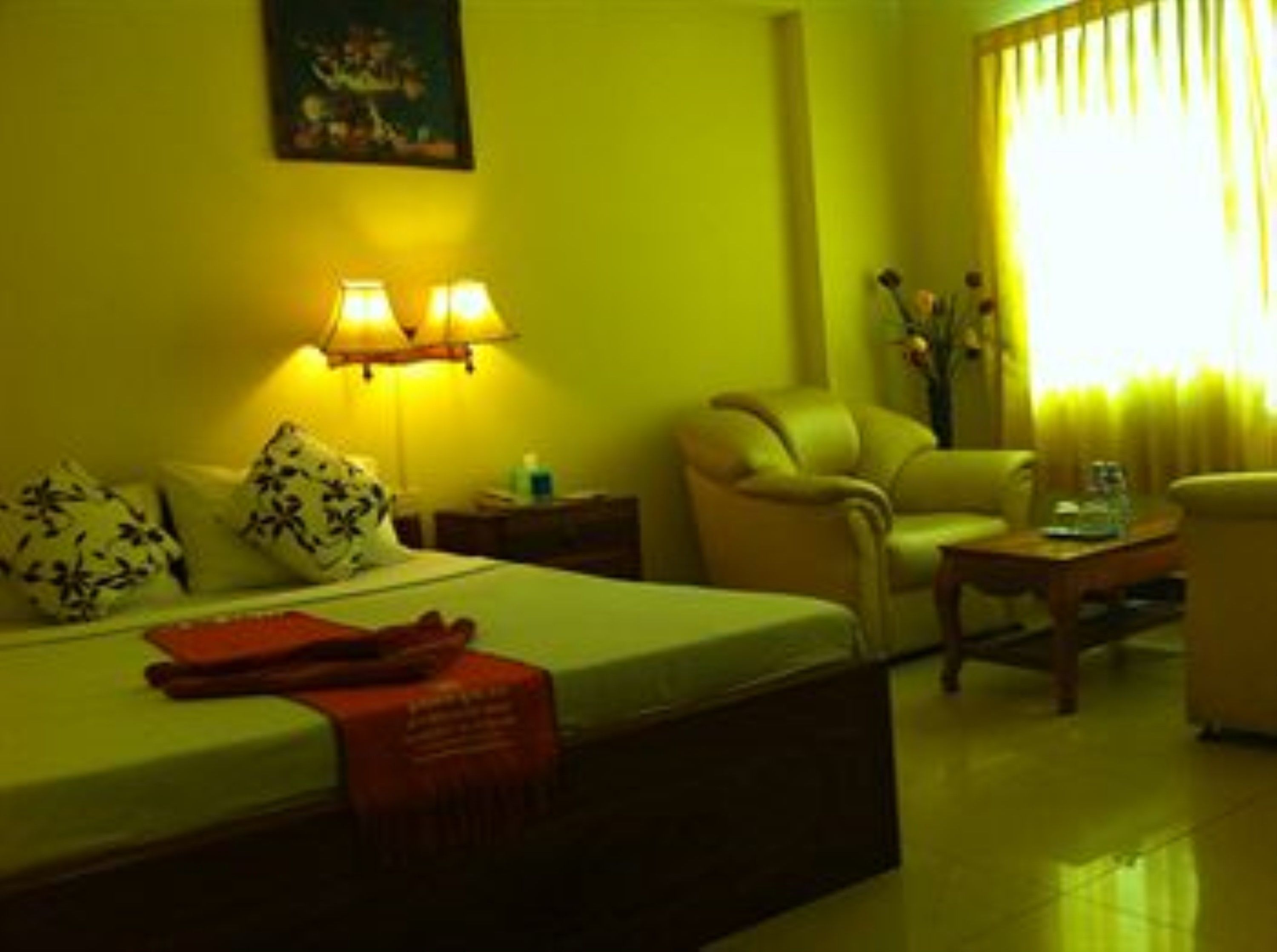 A hotel room with a bed, two bedside lamps, a chair, a small table, and a painting on the wall.