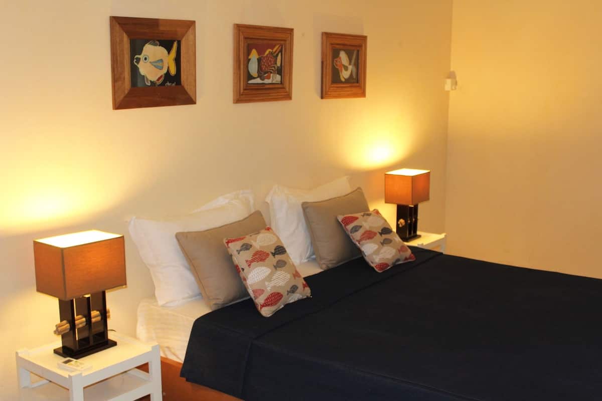 A bedroom with a bed, two bedside tables, lamps, and three framed artworks on the wall.