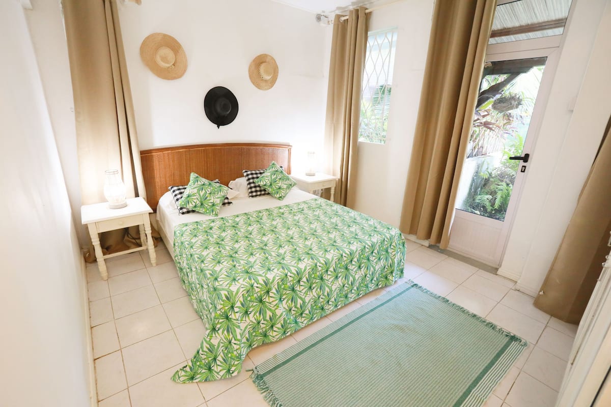 A bedroom with a bed, two nightstands, a window with curtains, and a view of greenery outside.