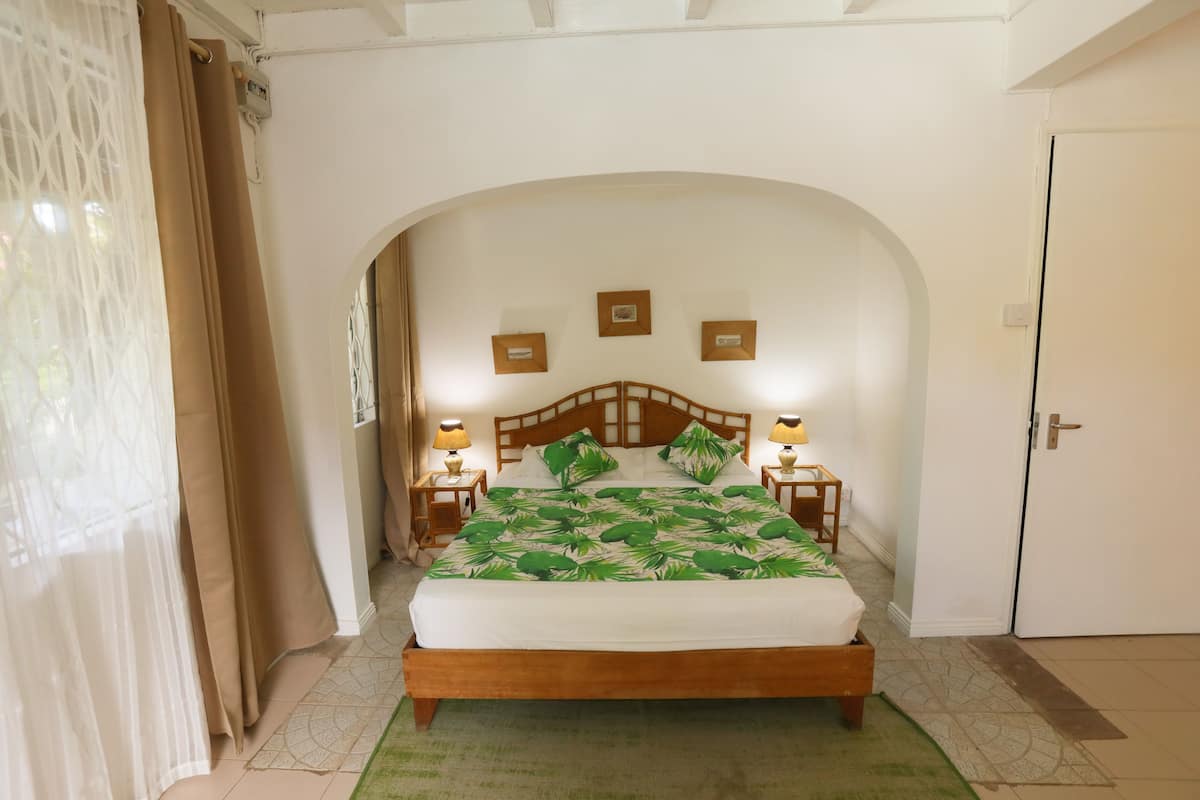 A bedroom with a wooden bed, two bedside lamps, a green and white patterned bedspread, and a white door.