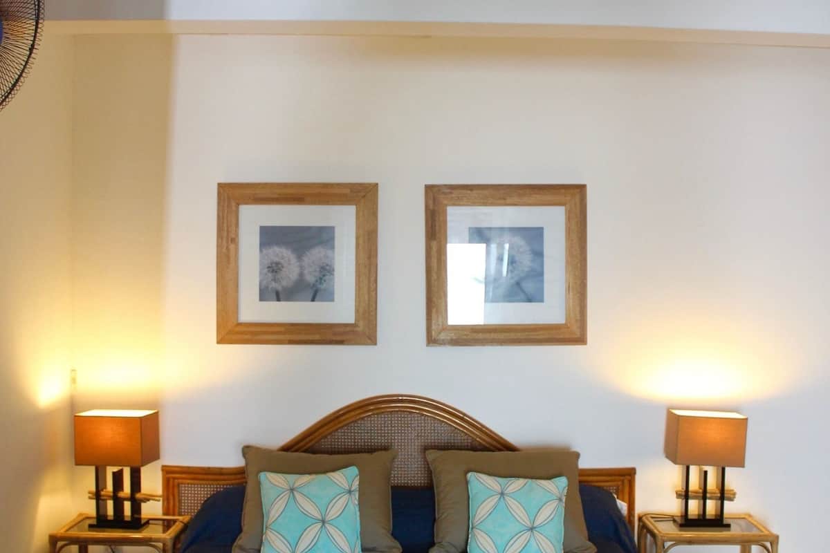 A bedroom with a bed, two bedside lamps, and two framed pictures on the wall.