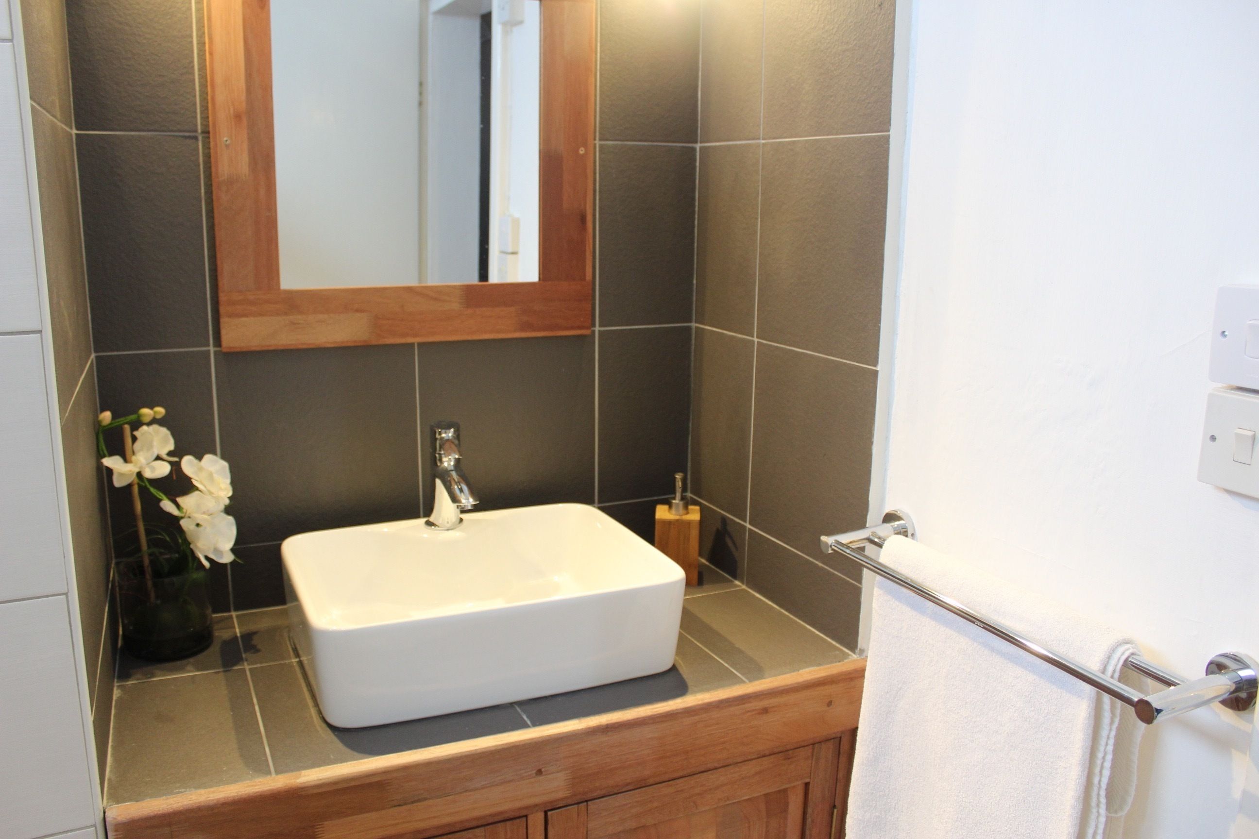 A bathroom with a white sink, wooden vanity, and a mirror above it.