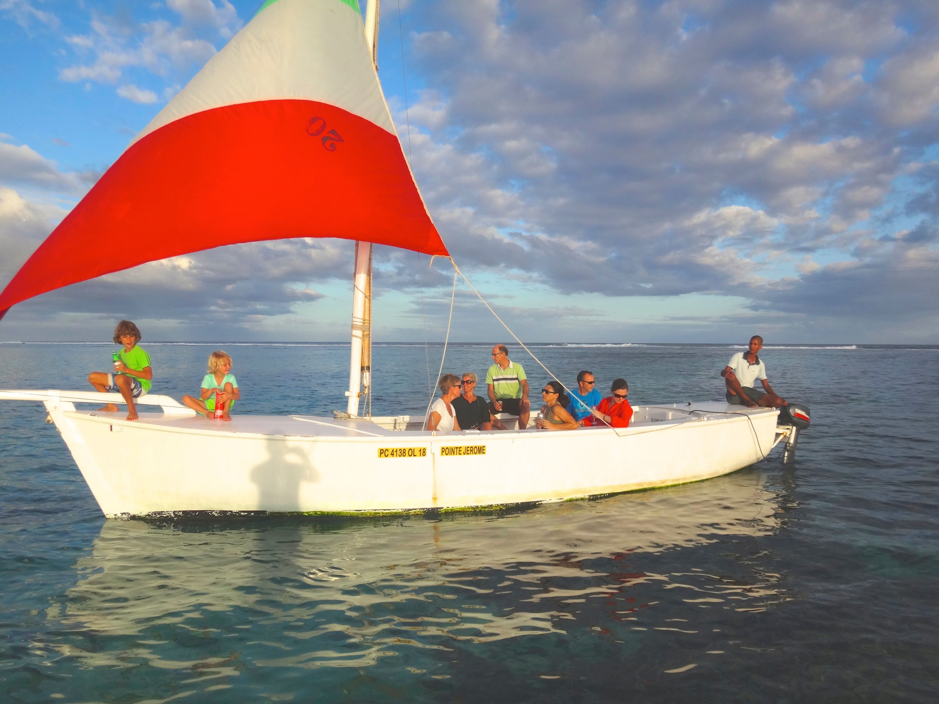 A boat with a sail, people on board, and calm water.