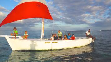 A boat with a sail, people on board, and calm water.