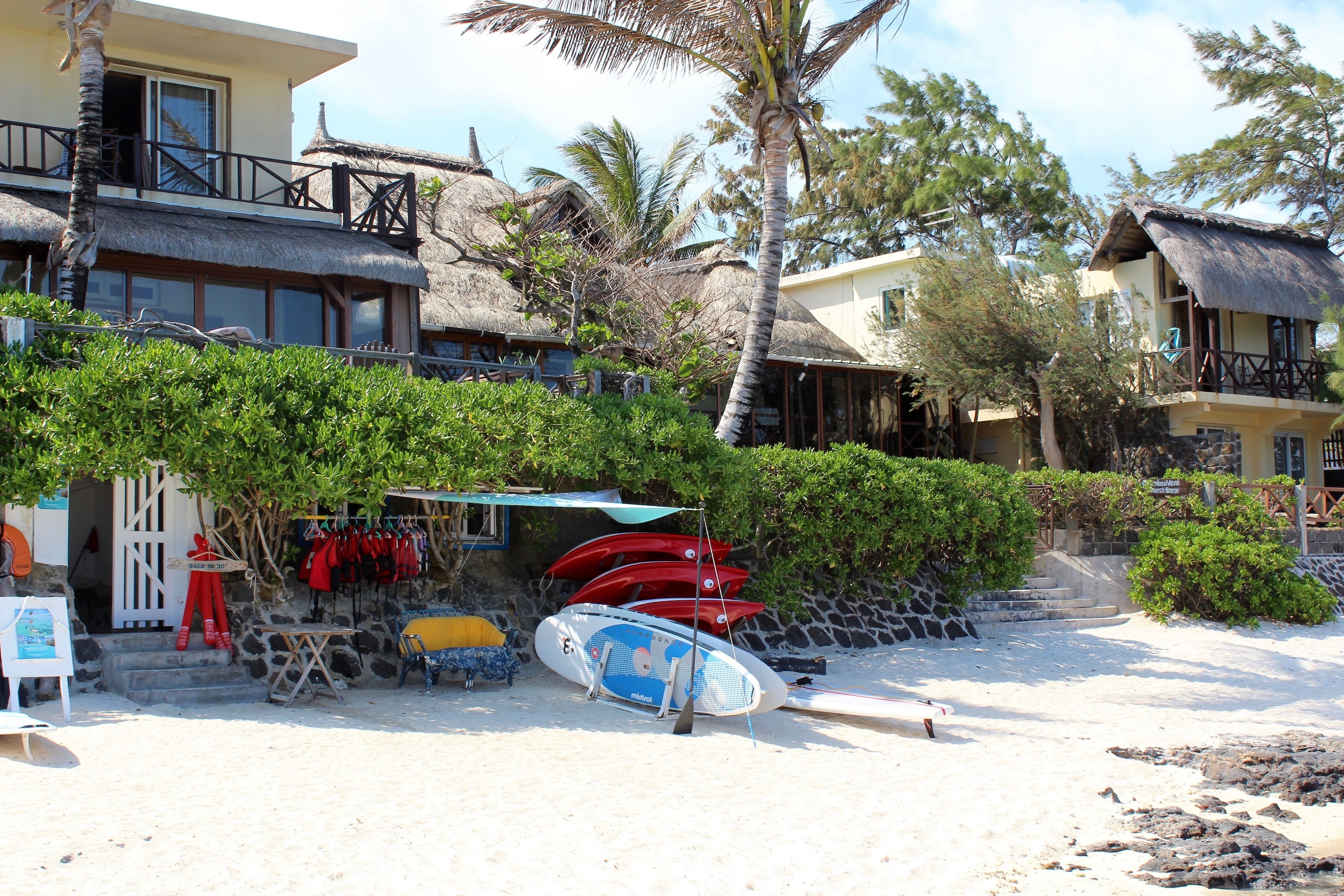 A beachfront property with thatched-roof buildings, a surfboard rental area, and a small shop.