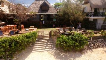 A guesthouse with a thatched roof, outdoor seating area, and a staircase leading to the entrance.