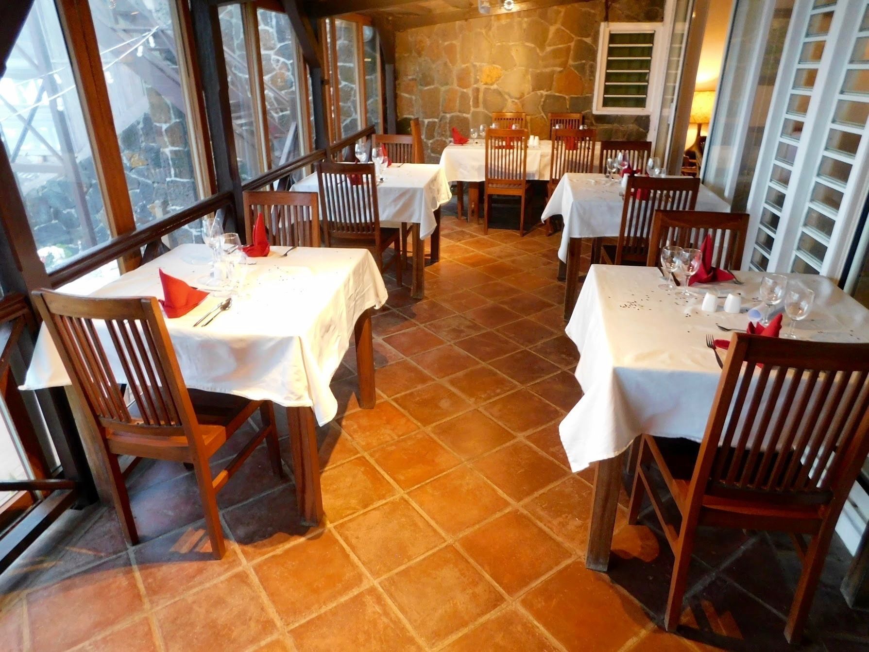 A restaurant with multiple tables and chairs, stone walls, and large windows.