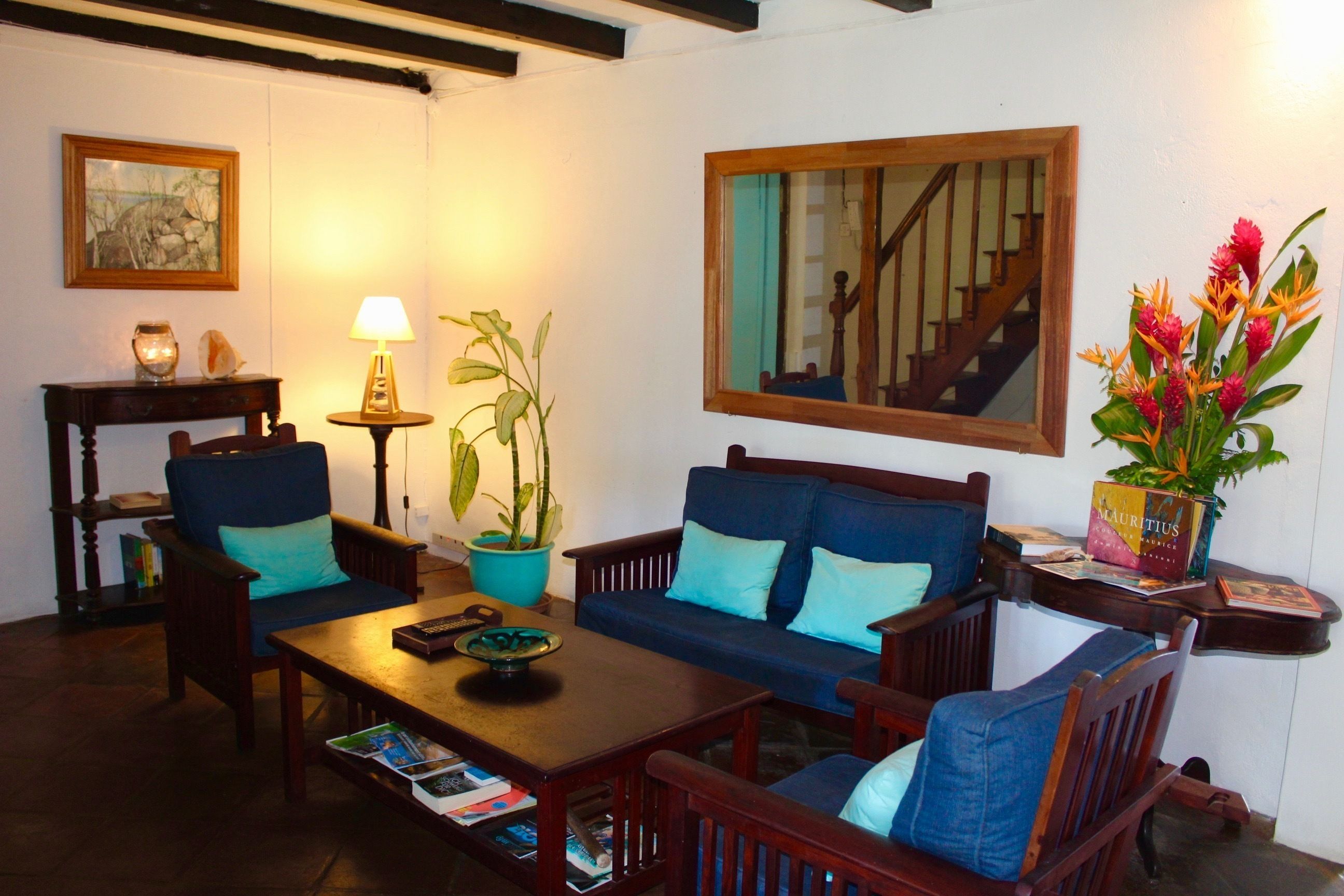 A cozy living room with a sofa, armchairs, a coffee table, a lamp, a potted plant, and a bookshelf.