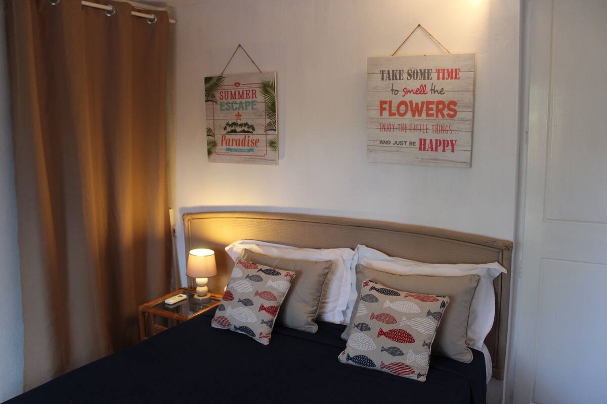 A neatly made bed with patterned pillows, a bedside lamp, and two inspirational wall art pieces.