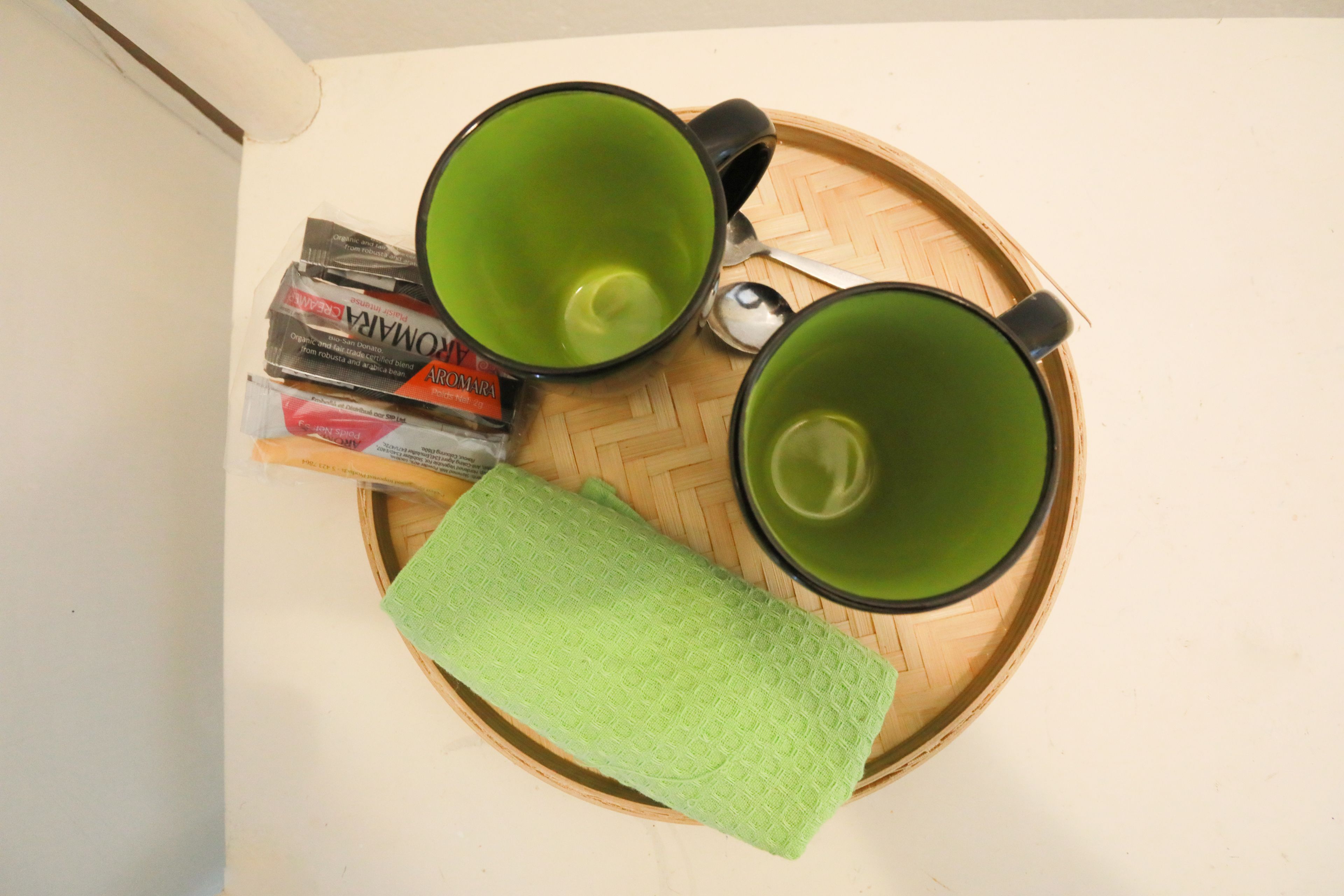 Dos tazas verdes sobre una bandeja de madera con un mantel verde, una cuchara y algunas revistas.