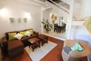 A living room with a brown sofa, wooden coffee table, and wicker chair. There is a dining area in the background with a table and chairs. - Chantauvent Guesthouse (Blue Bay)