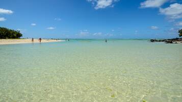 Una playa con aguas poco profundas y cristalinas, una orilla arenosa y algunas personas a lo lejos.