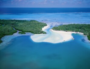 Vista aérea de una zona costera con playa arenosa, aguas azules cristalinas y vegetación verde densa.