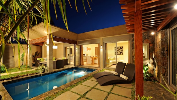 A modern outdoor pool area with a lounge chair, a dining area, and a stone wall.