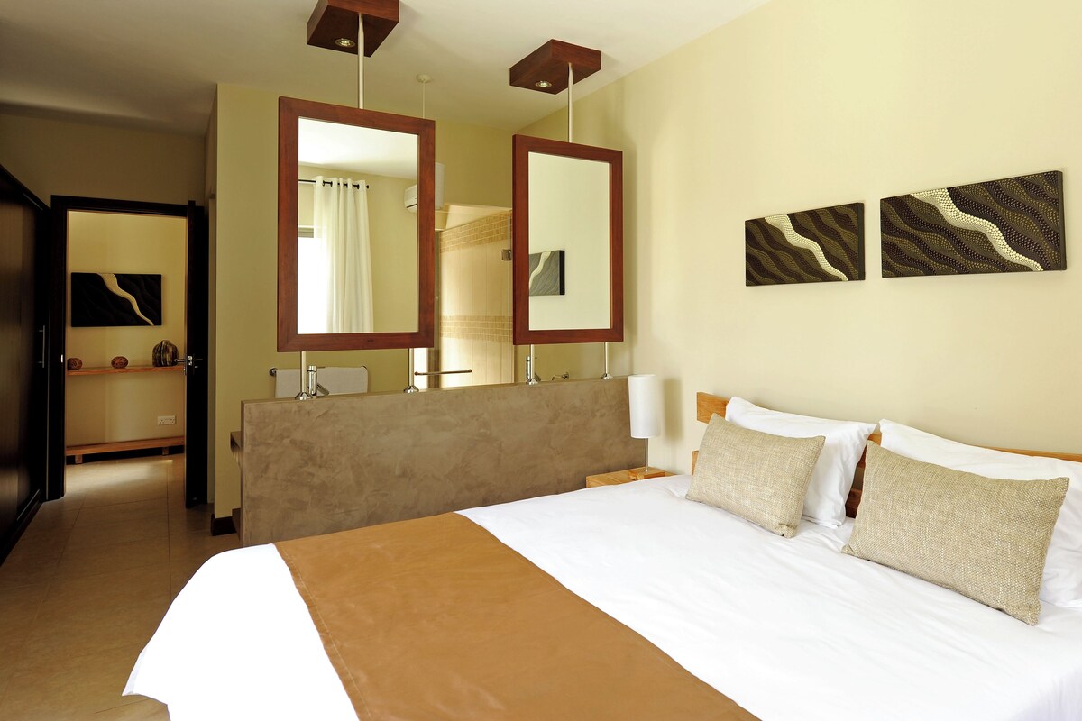 Habitación de hotel con una cama grande, dos espejos fijos en la pared, un cabecero de madera y dos obras de arte abstractas en la pared.