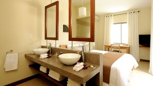 A hotel bathroom with a large mirror, two sinks, a vanity, and a bed.