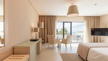 Habitación de hotel con cama, escritorio, sillas, televisor y balcón con vistas.