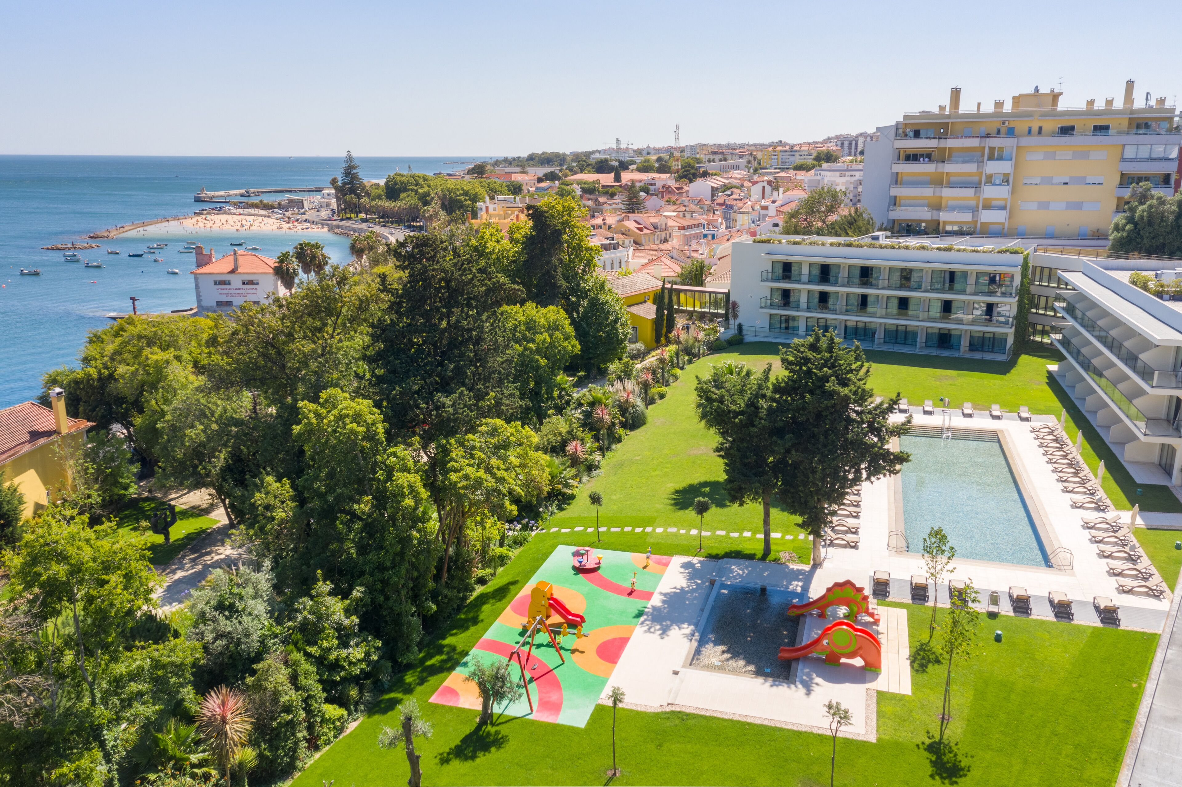 Vista aérea de una zona costera con playa, piscina y parque infantil.