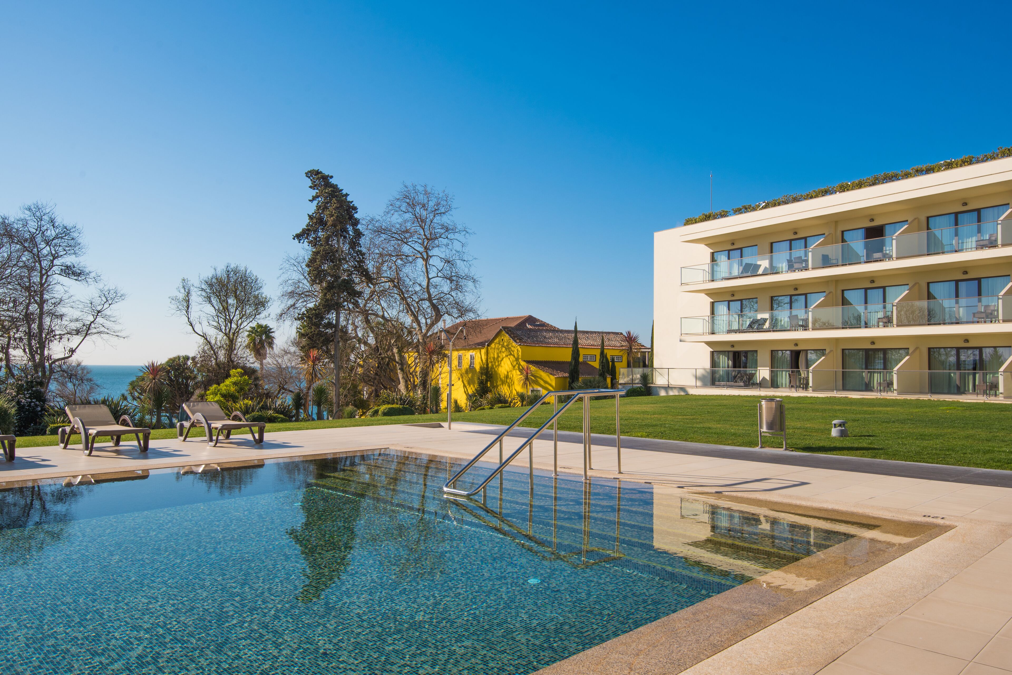 Une piscine d’un bleu éclatant, dotée de chaises longues, d’un escalier et d’un bâtiment avec des balcons.