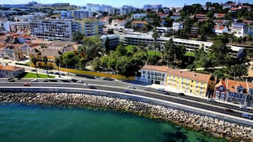Un paisaje urbano costero con un edificio amarillo destacado, un puerto deportivo y una carretera con vehículos.