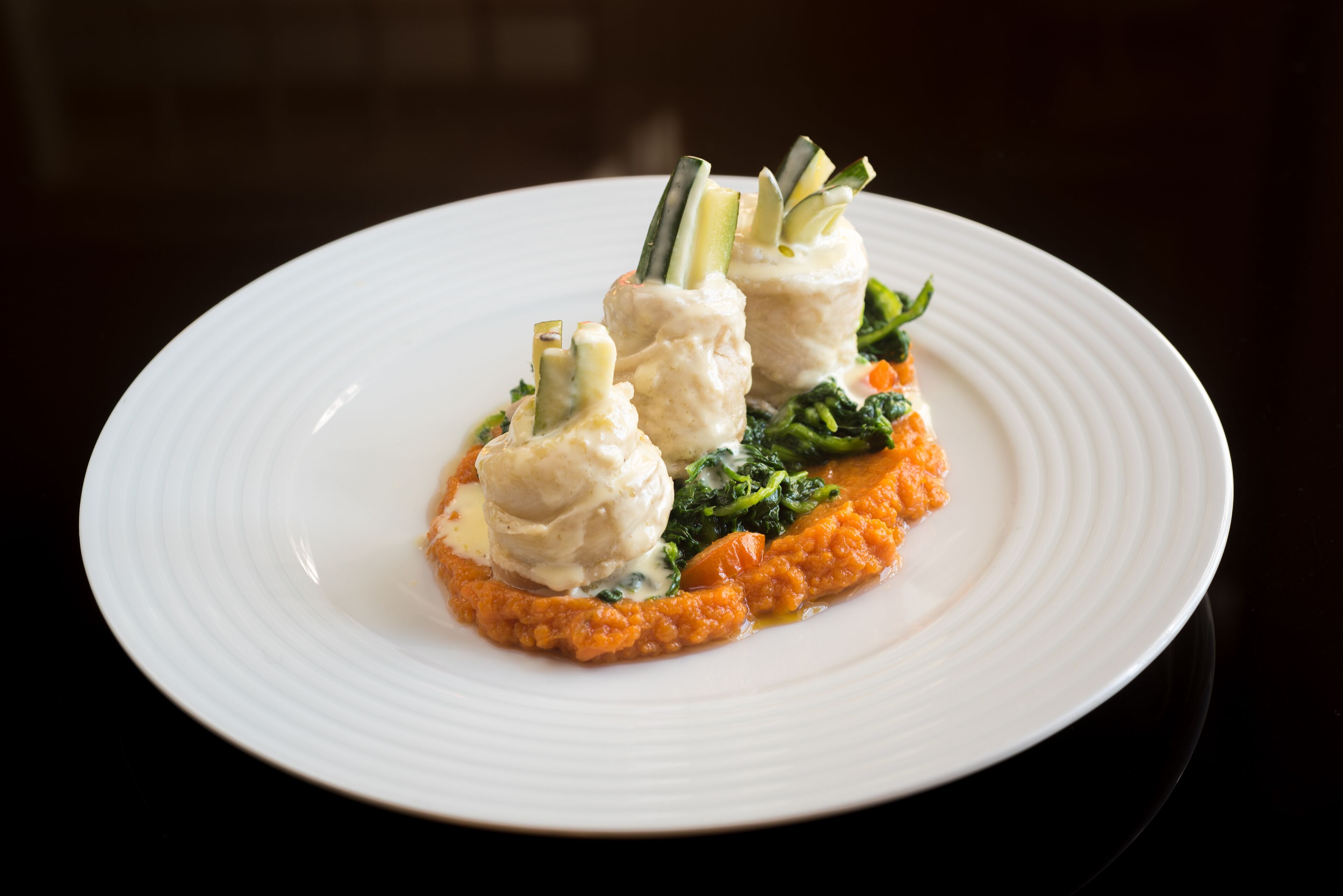 A white plate with a dish of food, including what appears to be dumplings and a puree, on a dark background.