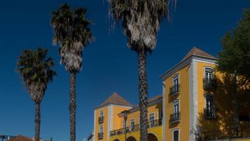 Un edificio amarillo con balcones y un techo rojo, rodeado de palmeras.