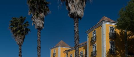 A yellow building with balconies and a red roof, surrounded by palm trees.