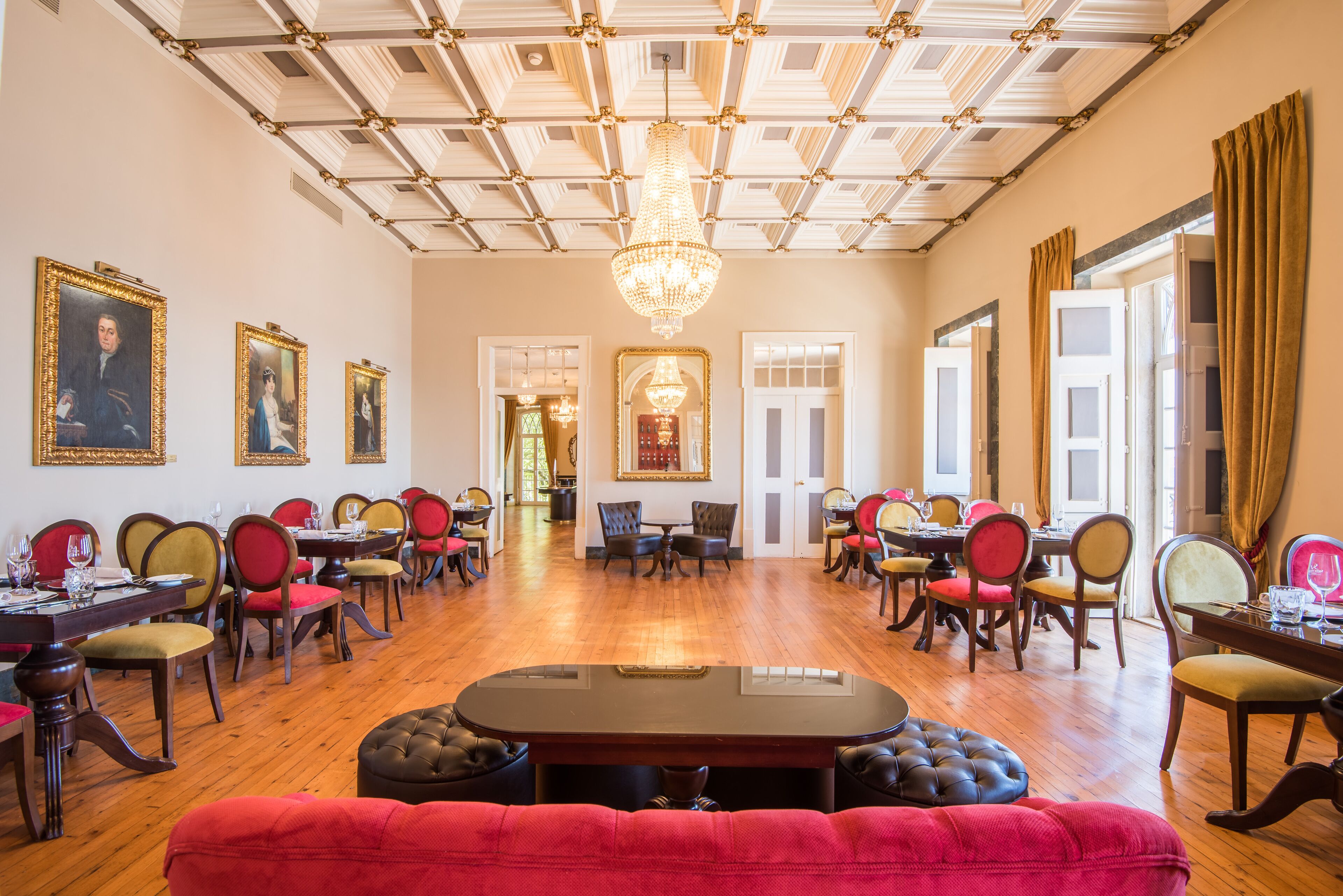 Un comedor amplio con varias mesas y sillas, un candelabro y retratos enmarcados en las paredes.