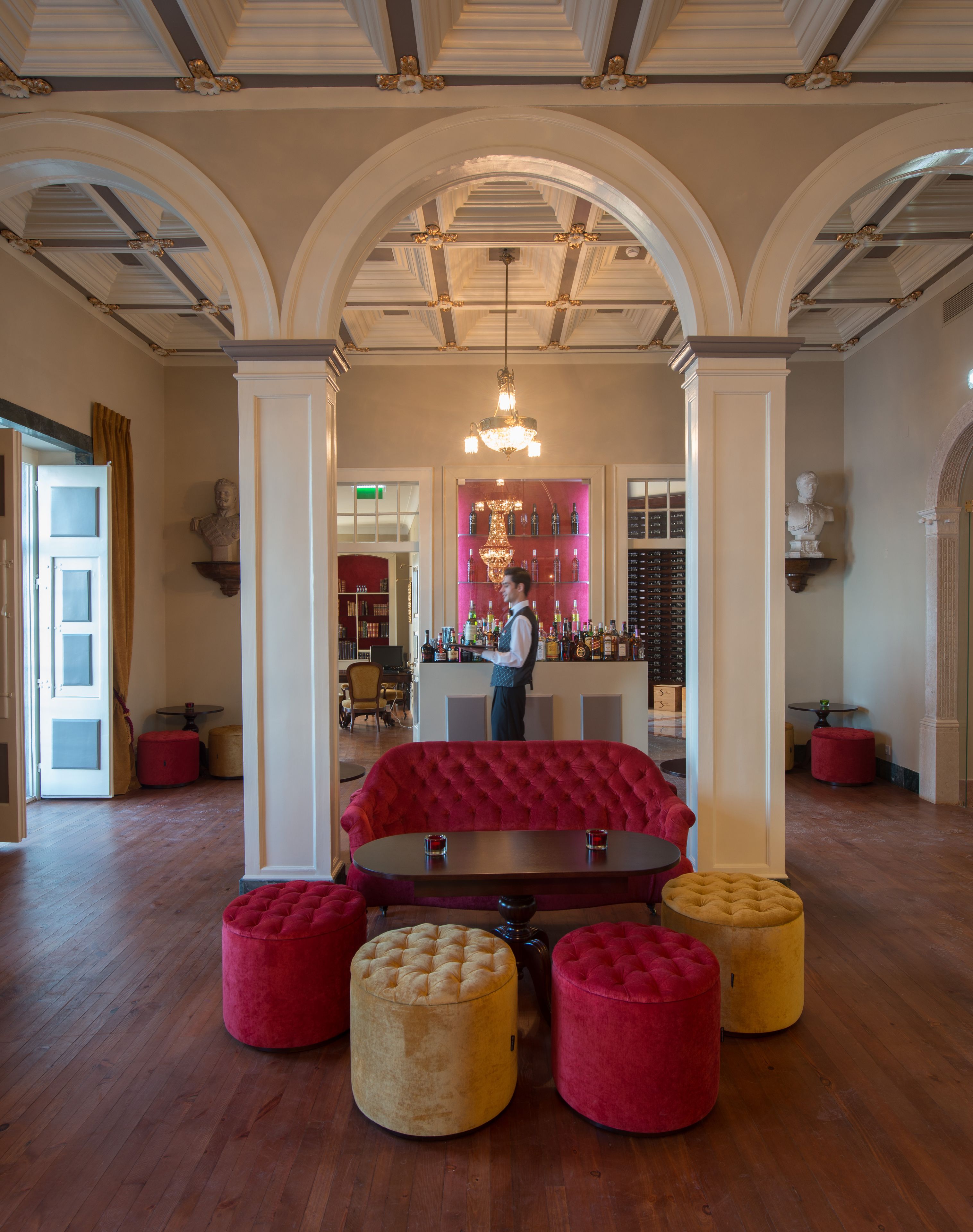 A lobby with a red tufted sofa, a bar area, and a chandelier.