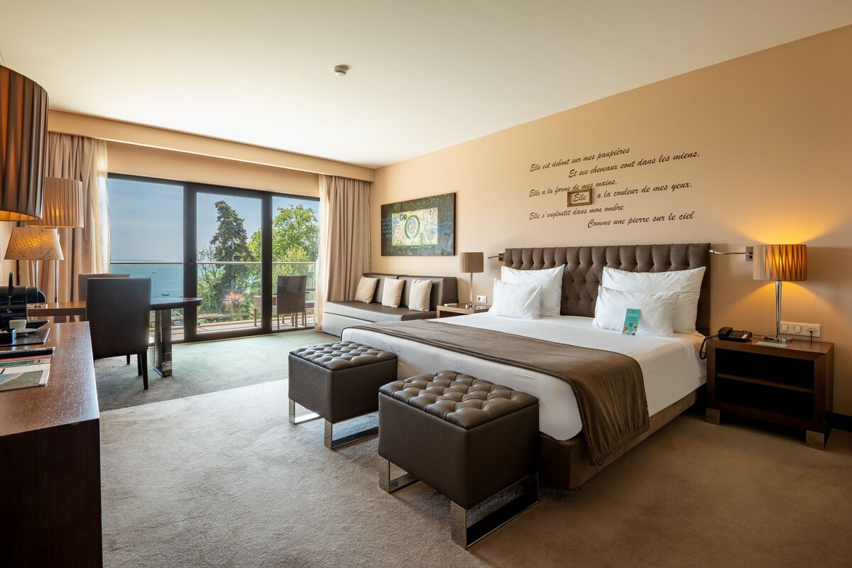 Camera d'albergo moderna con un letto grande, due poggiapiedi, una scrivania e vista sul mare.