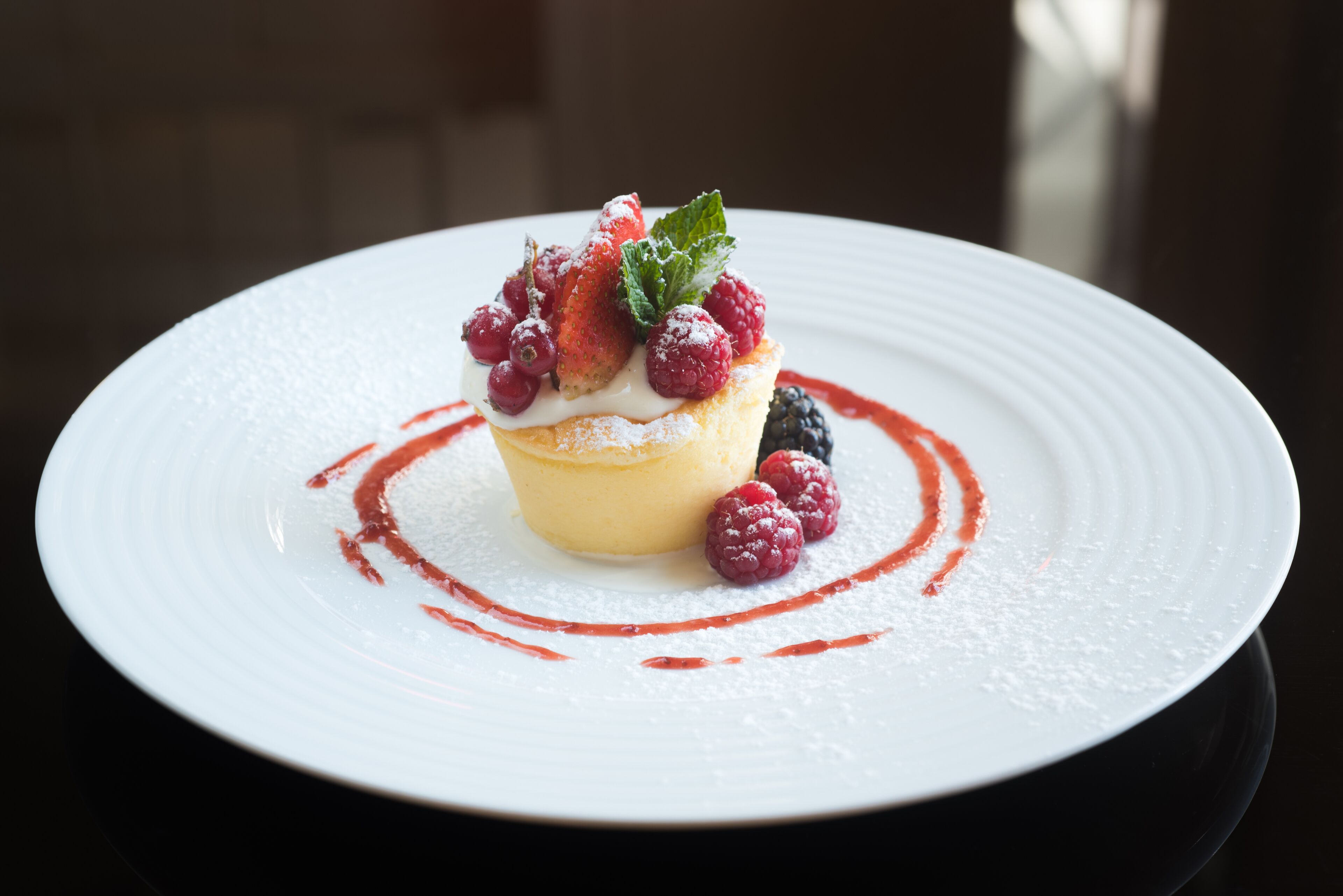 Un postre sobre un plato blanco con fresas, frambuesas y una hoja de menta encima.