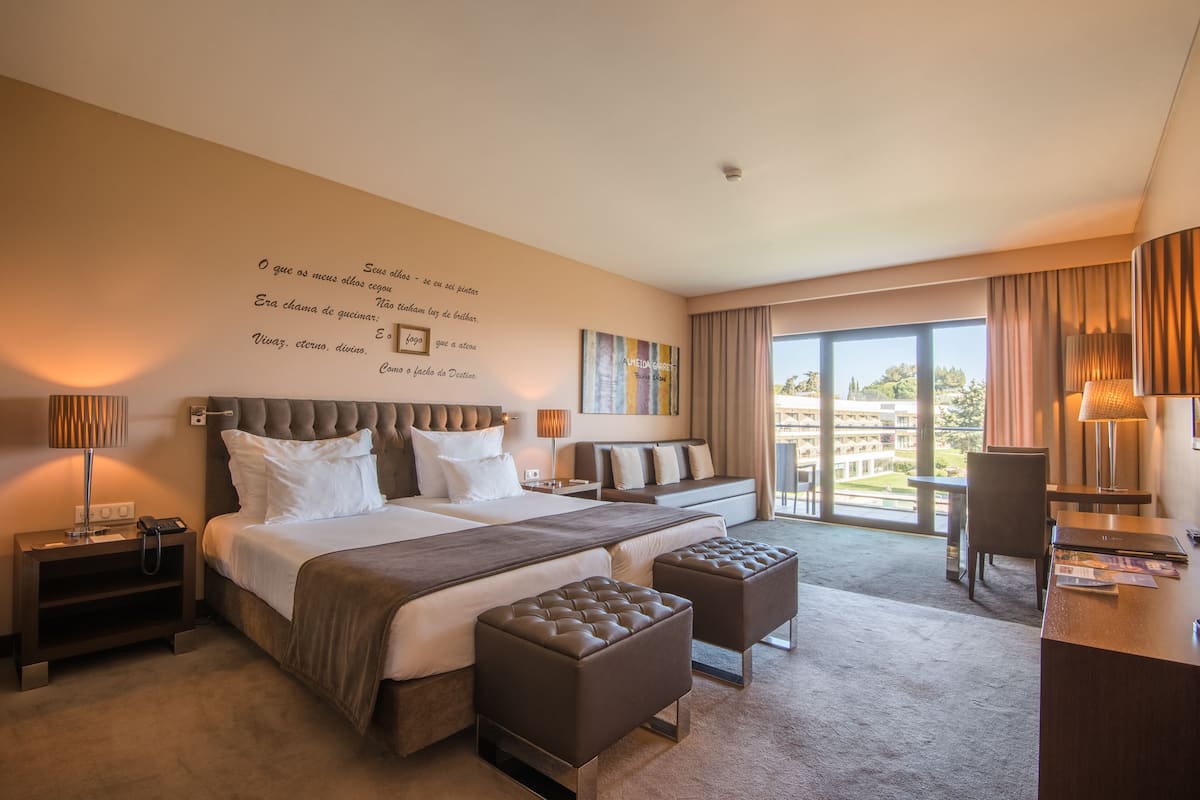 A spacious hotel room with a large bed, two bedside tables, a desk, and a view of the city.