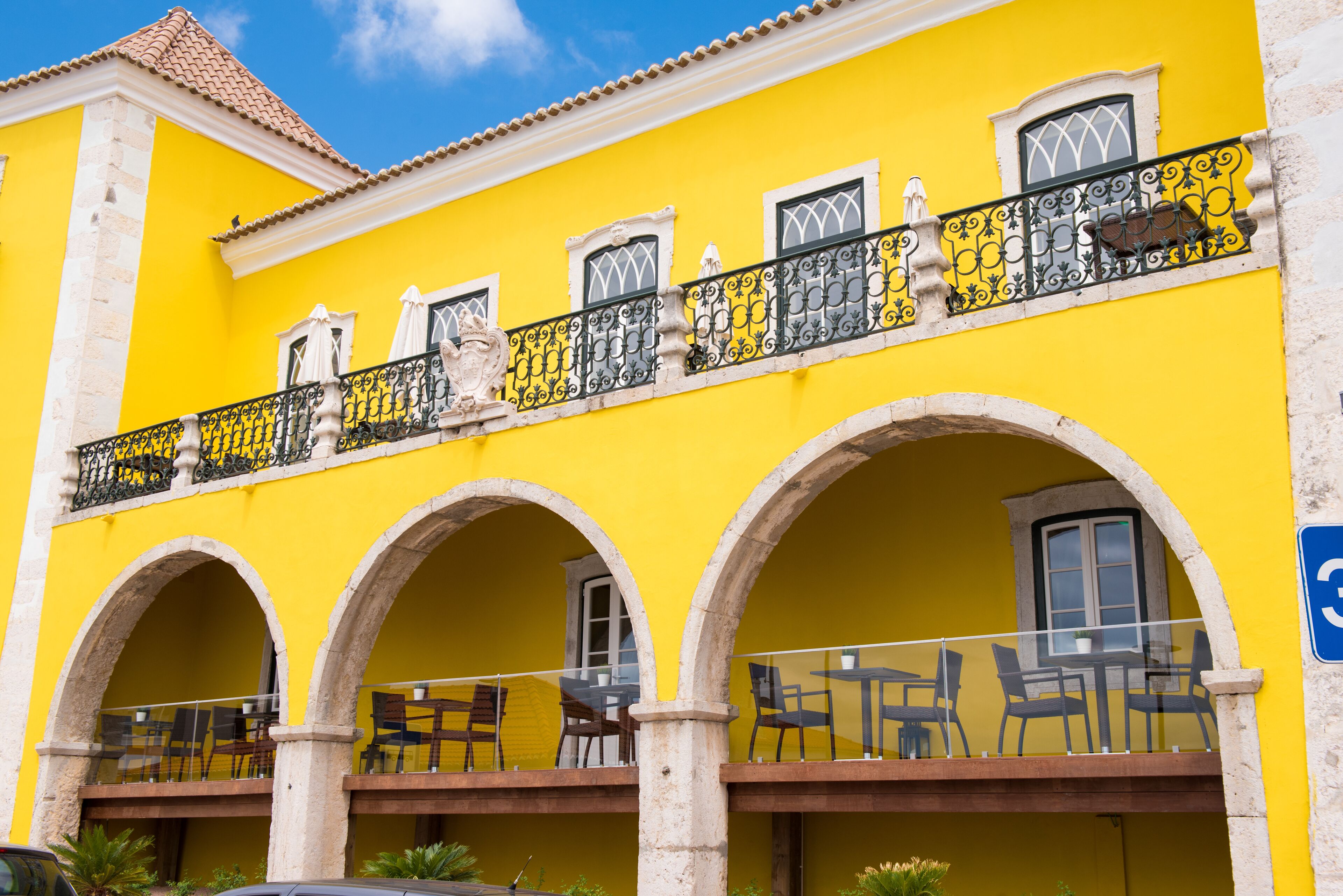 Um edifício amarelo com varanda, arcos e mesas ao ar livre.