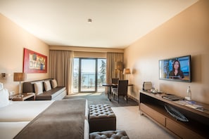 A hotel room with a bed, a desk, a television, and a view of the outdoors.
