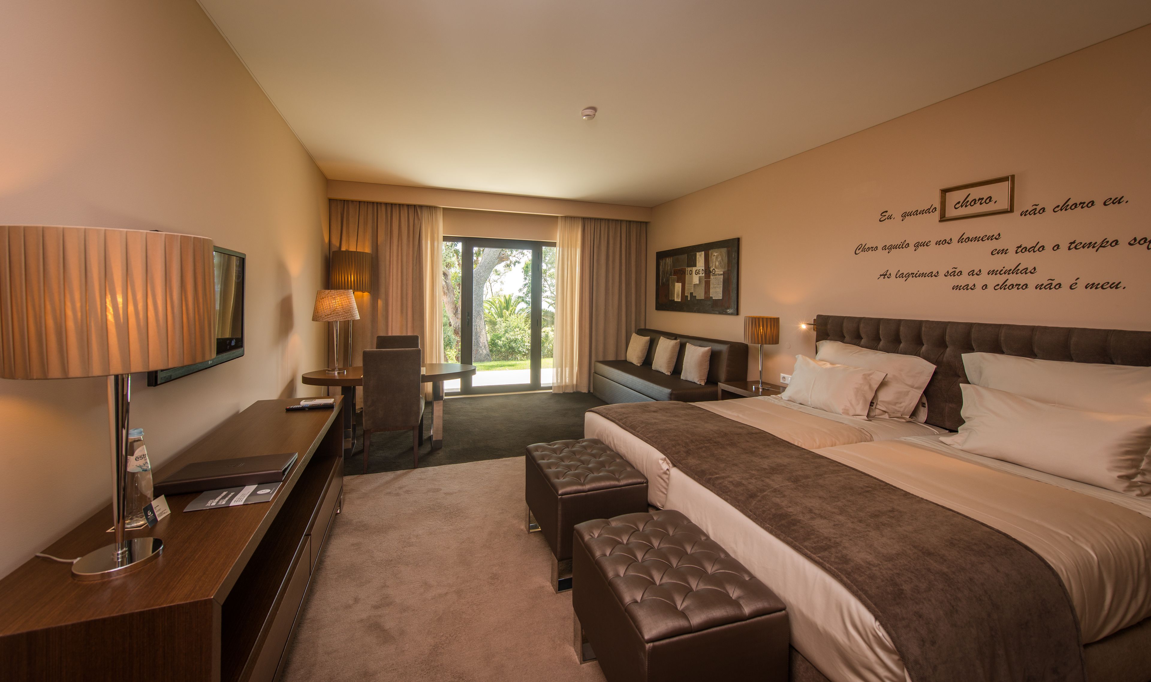 Ein Hotelzimmer mit Bett, Nachttischen, Schreibtisch, Stuhl, Lampe und Blick ins Freie.