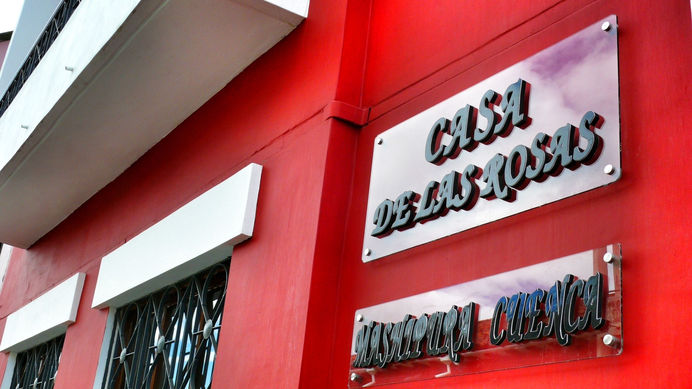 A building with a red exterior and two metal signs. One sign reads "CASA DEBOSQUES" and the other "MASCAPURA CUESTA".