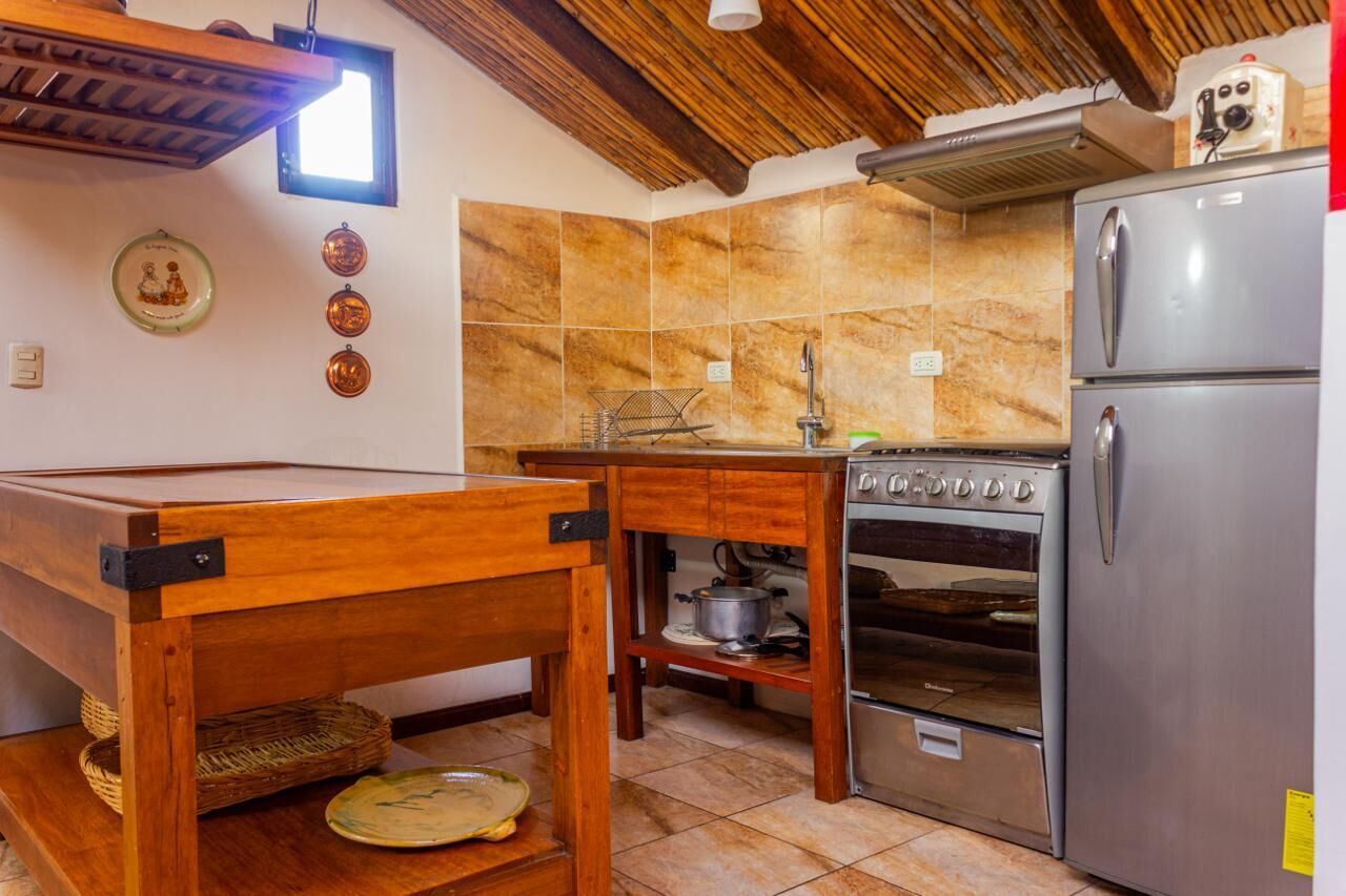 A kitchen with a wooden table, a stove, a refrigerator, and a tiled backsplash.