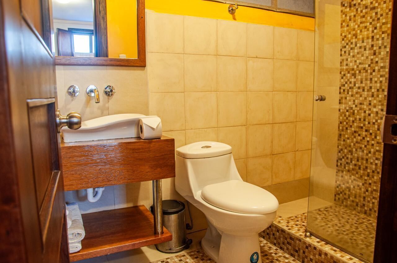 A bathroom with a white toilet, a wooden vanity, a sink, and a shower area with mosaic tiles.