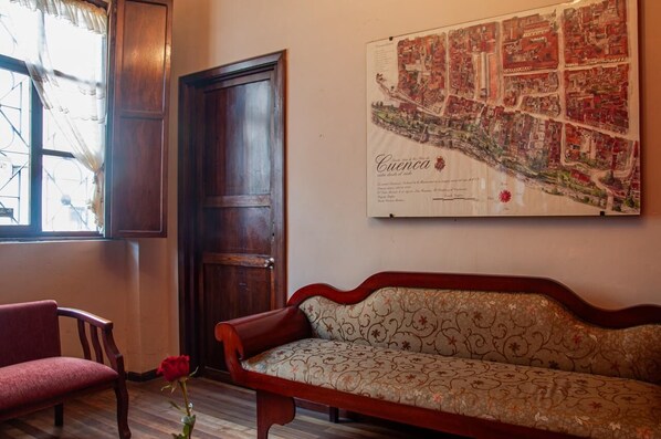 A room with a wooden door, a red chair, a sofa, and a map of Cuenca on the wall. - Casa de las Rosas (Cuenca)