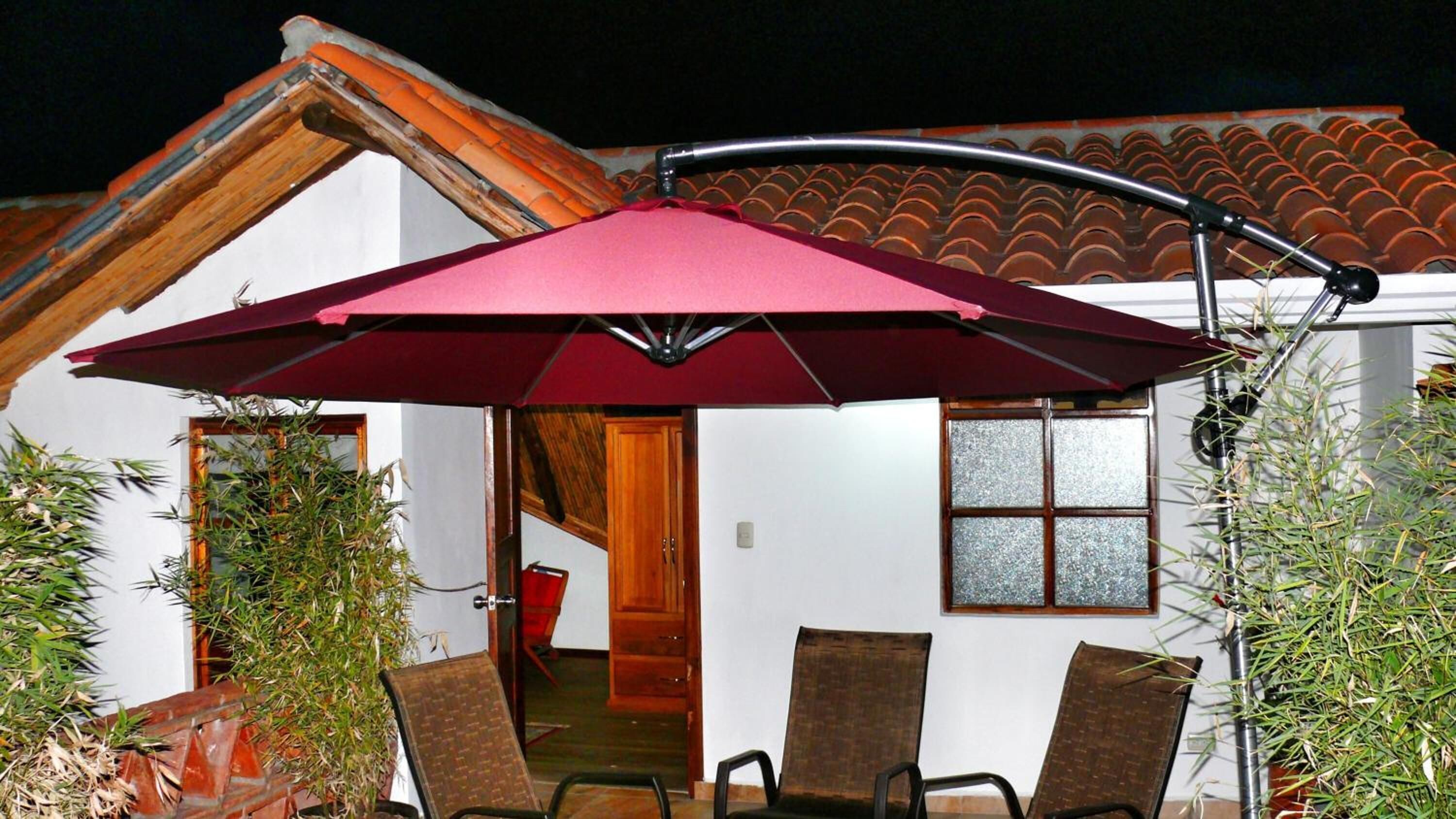 An outdoor patio area with a red umbrella, two chairs, and potted plants.