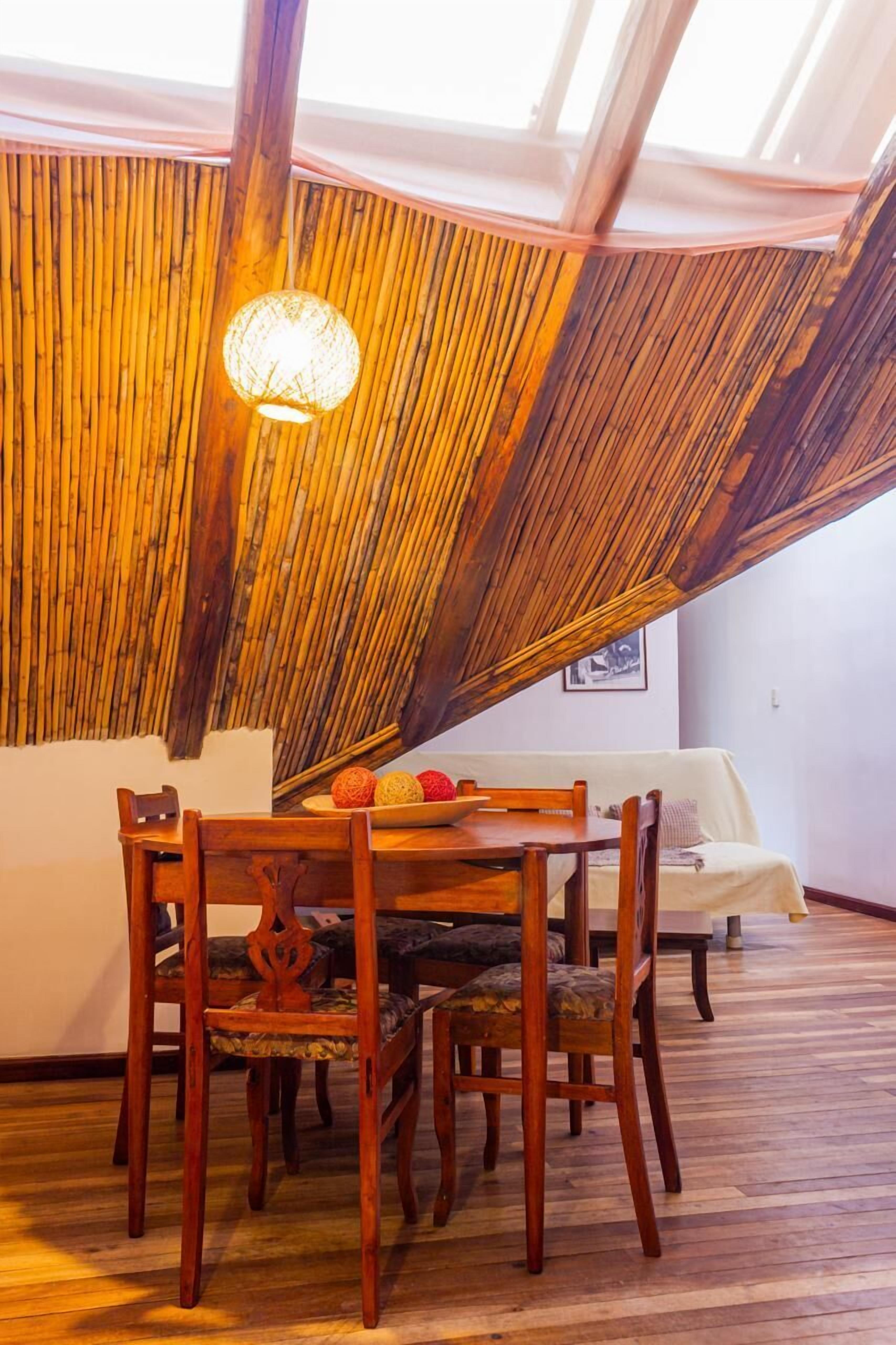 A dining area with a wooden table and chairs, a hanging light fixture, and a bamboo wall.