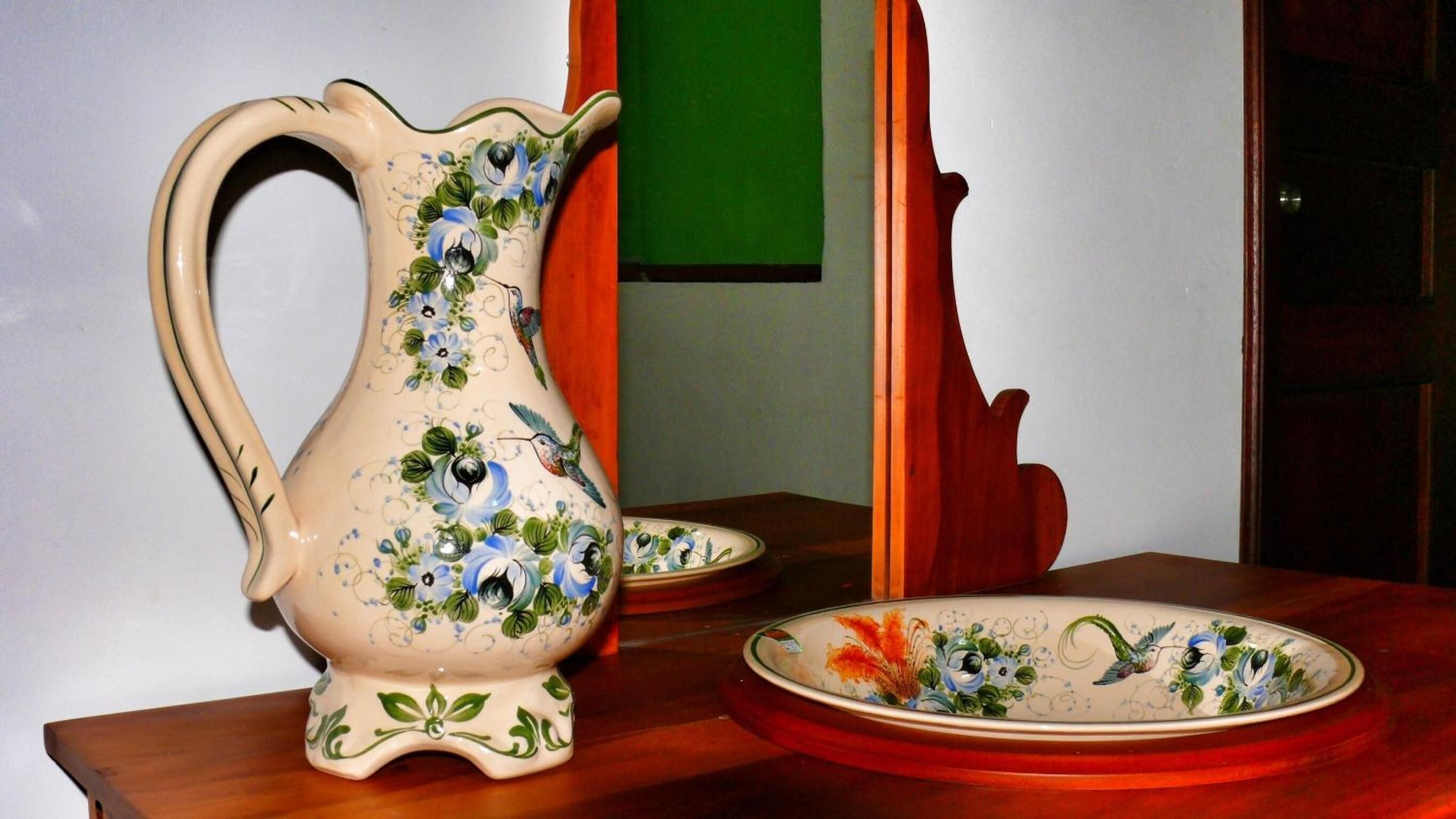 A ceramic pitcher with floral designs on a wooden table.